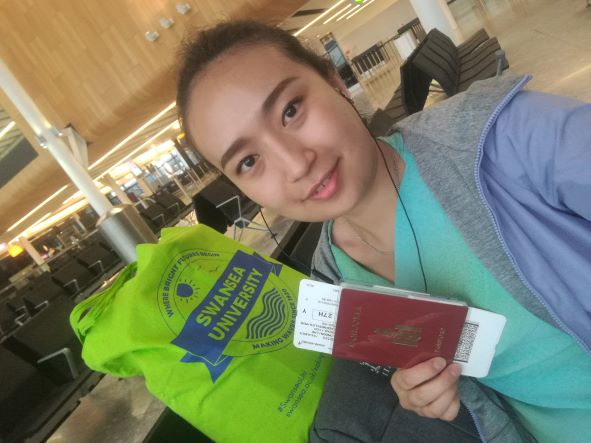 Student holding up passport with green Swansea University bag in the background