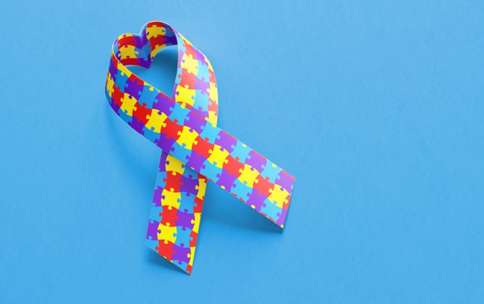 Ribbon featuring jigsaw pieces denoting autism awareness on a plain blue background