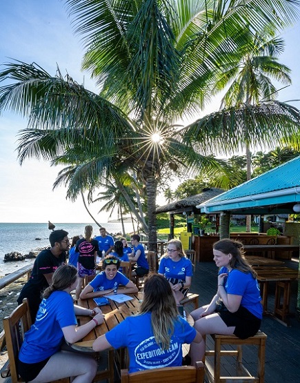 Students sitting in blue tops on beach in Fiji
