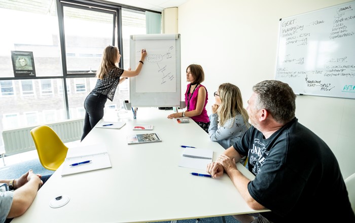 Adults in a room looking at a woman writing on a flipchart