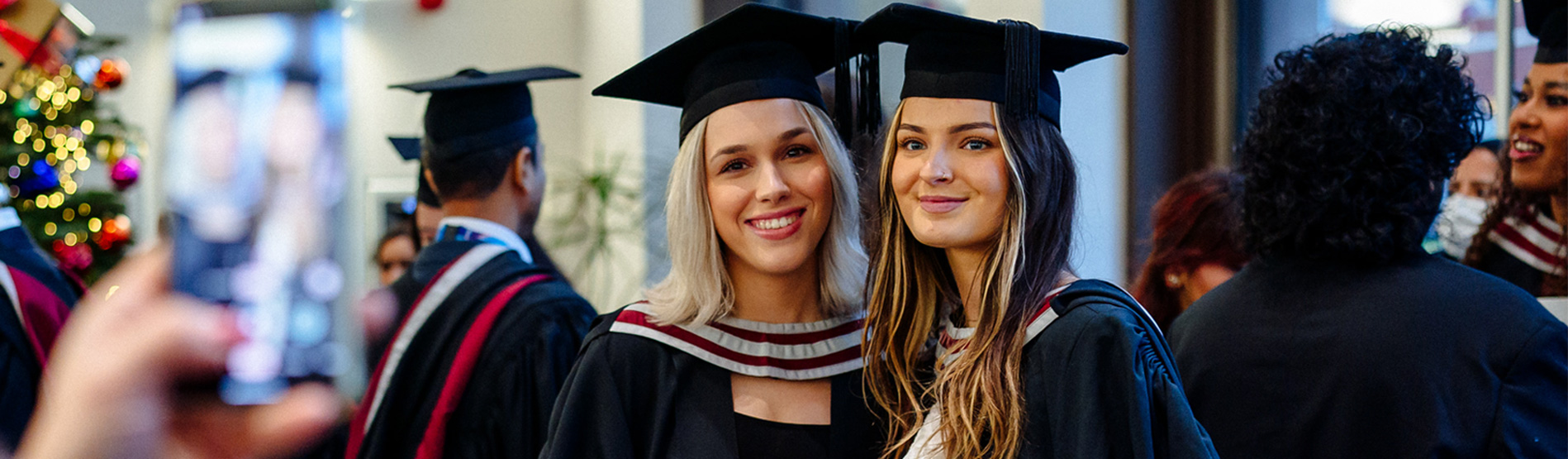 Two girls in their graduate gowns and hats are posing for a photo at their graduation ceremony