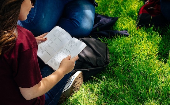 Student reading a book whist sitting on the grass