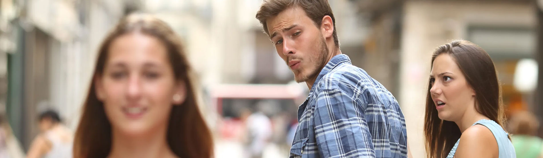 A couple walking down the street whilst the man looks back appreciatively of another woman.