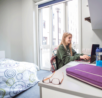 Photograph of a premium ensuite room on the Bay Campus with student sat on her laptop at the desk