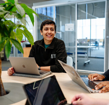 Three students with laptops sitting round a table chatting to each other