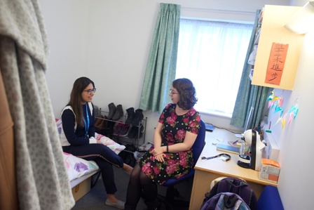 Two female students sitting in a student room, chatting and smiling