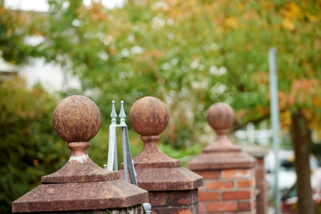 Red brick round pillar marking the end of a garden with Autumnal trees in the background