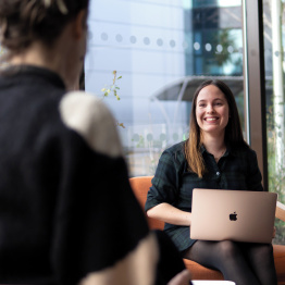 An image of a student studying at a laptop talking to another student on Singleton Campus.