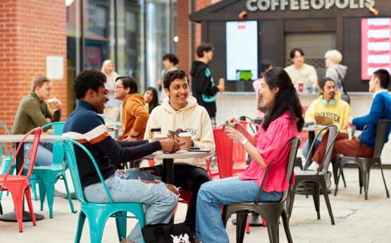 Three students sitting around table drinking coffee on university campus 