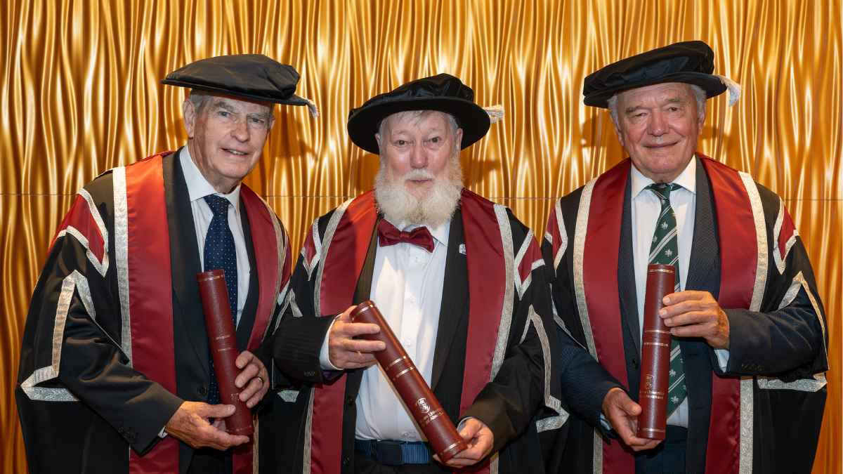 Three men wearing cap and gown and smiling at the camera