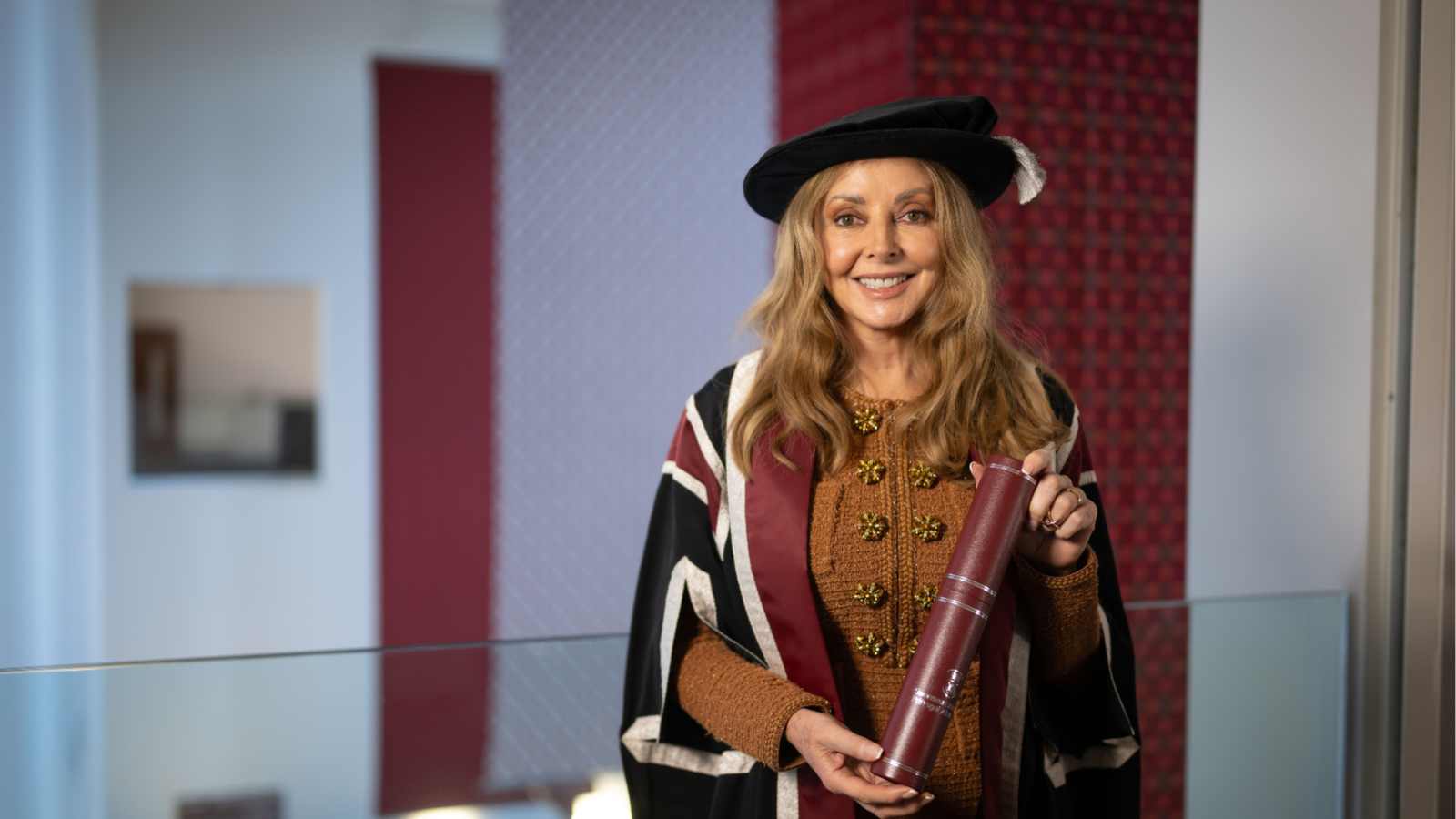 Lady wearing cap and gown, holding a scroll and smiling at the camera