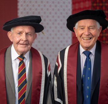 Two men dressed in cap and gown smiling at the camera