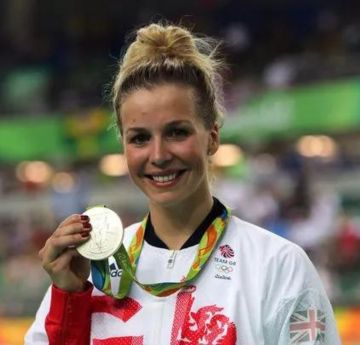 Lady in a stadium holding up an Olympic Medal.