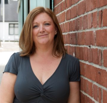 Woman standing with a shoulder against a wall smiling at the camera
