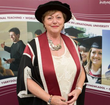 Lady in a cap and gown holding a scroll smiling at the camera