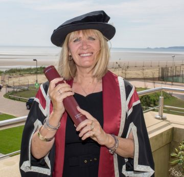 Woman standing on a balcony wearing cap and gown wearing and holding a scroll