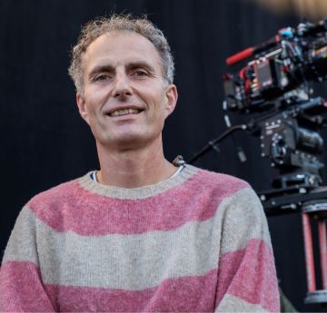 Photo of man with a film camera behind him smiling