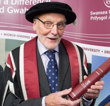 Man wearing cap and gown holding a scroll smiling at the camera