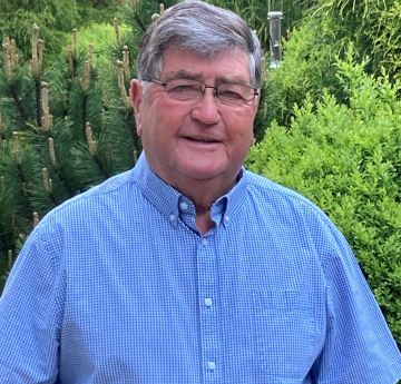 Man standing outside in front of a greenery smiling at the camera