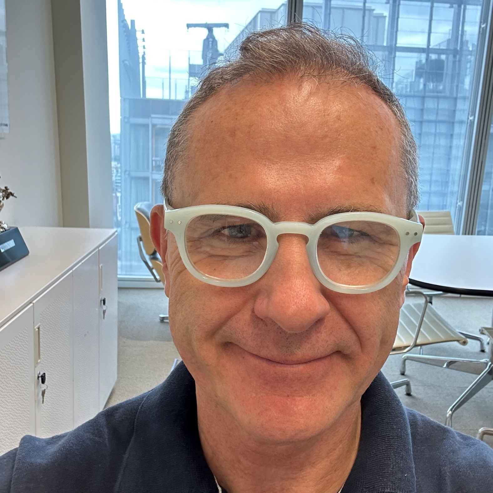 Man wearing glasses, sitting in an office smiling at the camera 