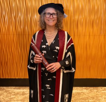 Lady in cap and gown holding a scroll smiling at the camera