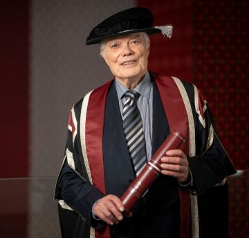 Man holding holding a scroll and cap and gown looking at the camera