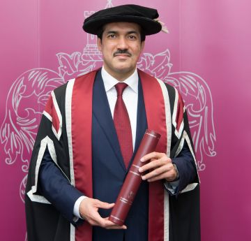 Man in cap and gown holding a scroll smiling at the camera