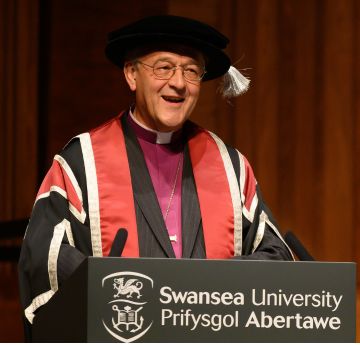 Man wearing cap and gown standing at a lectern making a speech