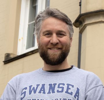 Man wearing a Swansea University hoodie smiling at the camera in front of the Abbey