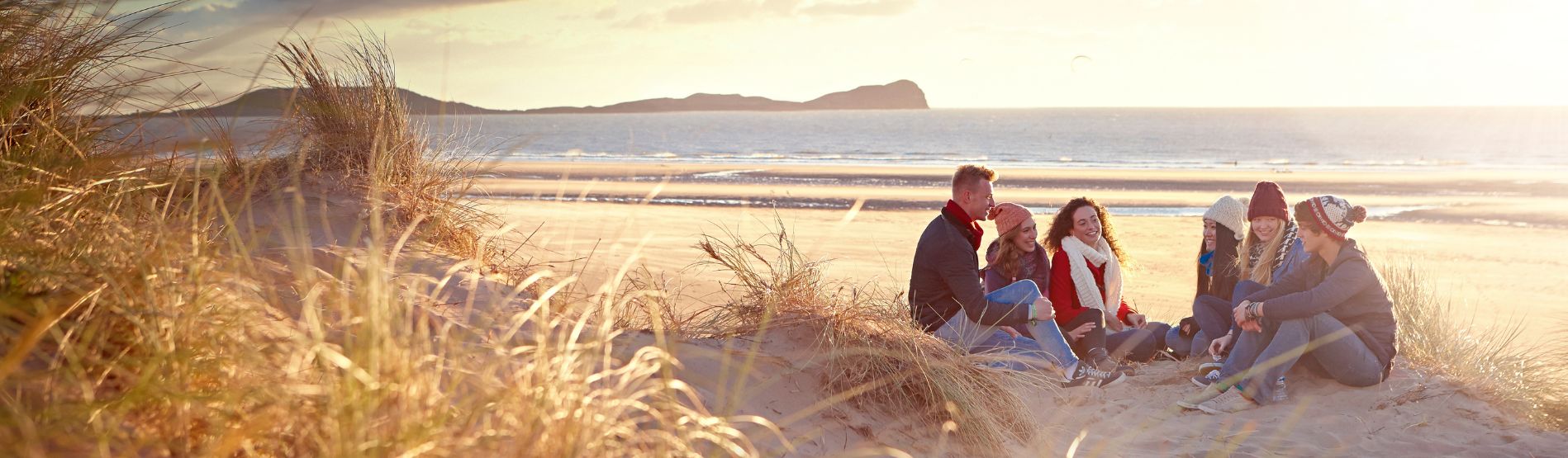 Students sitting on a beach smiling with the coast behind them