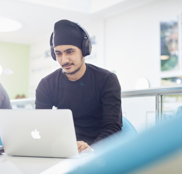 Male student wearing headphones sat at a laptop