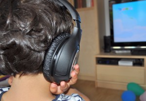 Image of a child wearing over ear headphones and looking at a television 