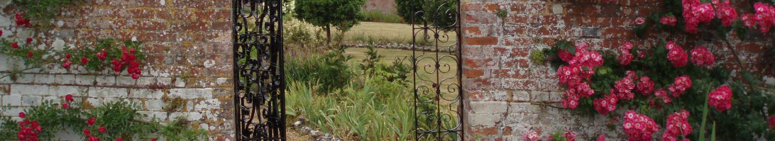 Image of an open gate set in a stone wall, leading out to gardens and grassland. 