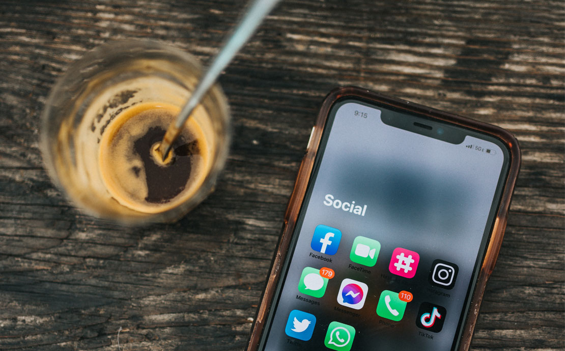 Image of a phone screen with social media apps and a glass of coffee by it