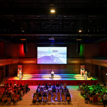 Looking down at delegates at an event in the great hall, sitting in rows listening to different speakers on stage via headphones