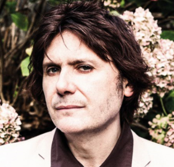 Image of Nicky Wire in a white suit in front of flowers
