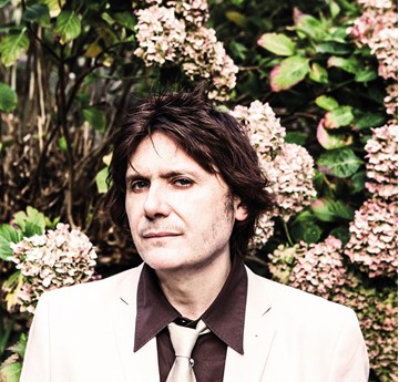 Nicky Wire in a white suit in front of flowers