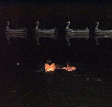 Two students in the pond at night, swimming towards the swan boats