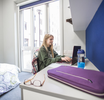 Female student in halls of residence, sitting at a desk on a lap top.