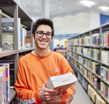 Male student in the library holding a pile of books.