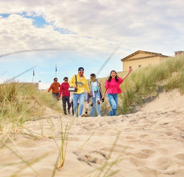 An image of a group of students walking onto the beach next to Bay Campus.