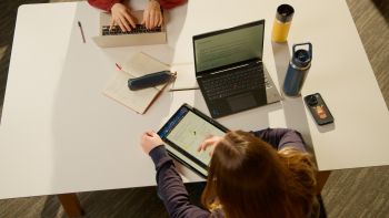 An image of a student working at a desk with a laptop and tablet device.