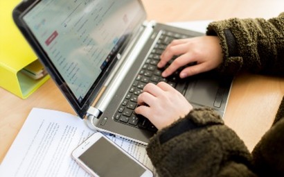 An image of a student studying and typing on a laptop.