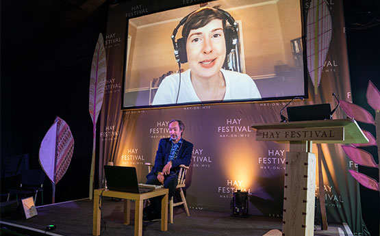 Alan Bilton seated onstage at Hay festival, Patricia Lockwood pictured on large screen above.