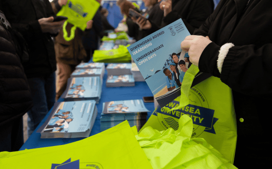 Myfyrwyr y dyfodol yn pigo lan prosbectws mewn ffair myfyrwyr. 