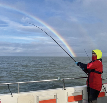 Gwraig ar gwch ar y môr gyda gwialen bysgota fawr