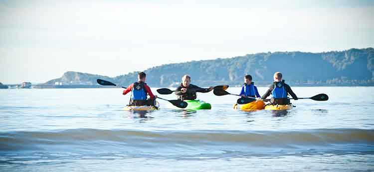 A group of students on kayaks in Swansea Bay with Mumbles in the background