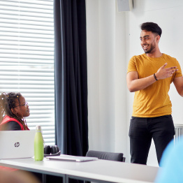 Delwedd o fyfyriwr yn cyflwyno mewn ystafell seminar.