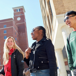 Delwedd o dri myfyriwr yn cerdded trwy Ganolfan y Bae heibio adeilad Tŵr y Cloc.