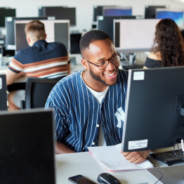 Delwedd o fyfyriwr yn gweithio ar gyfrifiadur mewn lab PC.